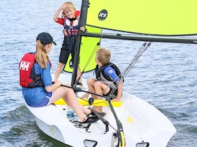Jungendliche segelt mit zwei spielenden Kindern mit der Segeljolle RS Zest bei wenig Wind