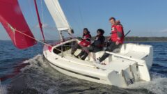 Drei Erwachsene segeln ihren Aira 22 Daysailer unter Gennaker mit Krängung bei Mittelwind und schneller Fahrt - Blick von schräg achtern ins Kockpit.